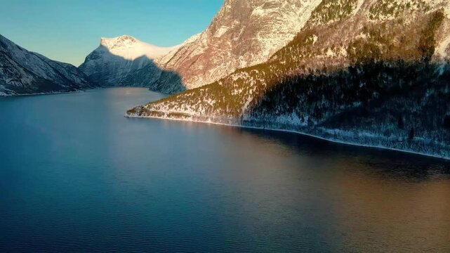 aerial footage captures the serene beauty of a snow covered Norwegian fjord, likely in the Eresfjord or Eikesdalen region, during winter.