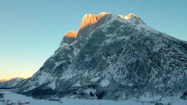 aerial footage capturing the majestic snow covered mountains of Eikesdalen or Eresfjord, Norway, bathed in the warm, golden light of sunrise or sunset.