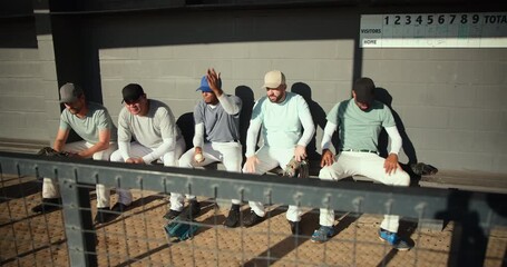 Leaning to whisper, five male baseball players drumming gloves tying cleat watching game in dugout - Powered by Adobe