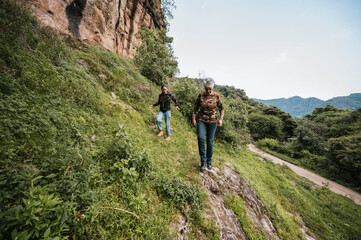Fototapeta premium Mother and daughter dressed in hiking clothes, walking along a trail in the middle of the rainforest. 
