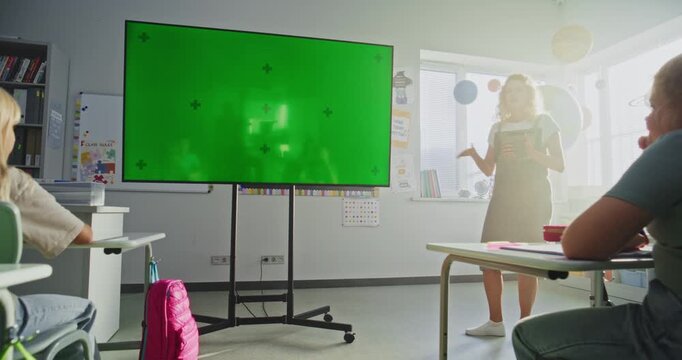 Modern Classroom: Female Teacher with Tablet Computer Teaching Primary School Children Using Digital Screen with Chromakey Mockup. Green Screen Placeholder for Interactive Visual Effects. Dolly Shot.