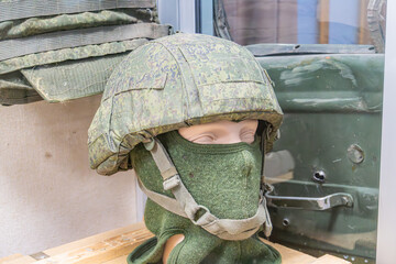 Display of military equipment Helmeted mannequin with camouflage pattern, additional equipment on helmet sides Background dark military vehicle door structure Artificial lighting No visible text