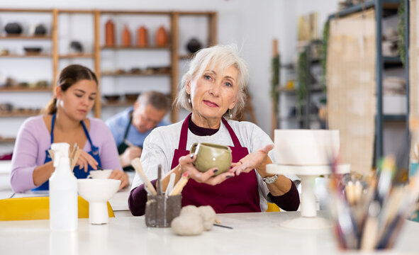 Satisfied elderly woman demonstrates pottery made by her own hands - Powered by Adobe