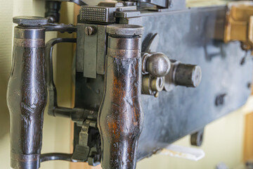 Close-up view of an aged metal mechanical device with handles and a control knob, set against a light-colored interior wall