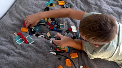 Child in eyeglasses assembling colorful construction toy pieces on comfortable couch during playtime at home. STEM learning, fine motor skills development and independent creative activities. 