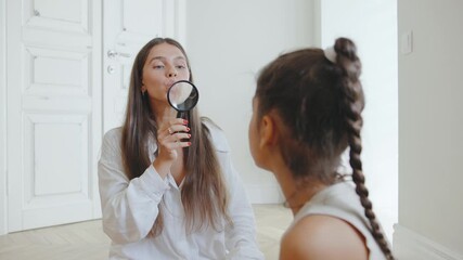 Speech therapist conducting a session with young girl using a magnifying glass mirror to aid communication skills in a bright, modern room - Powered by Adobe