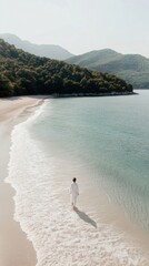 Solitude on a serene beach: person walking along calm shoreline with mountain backdrop