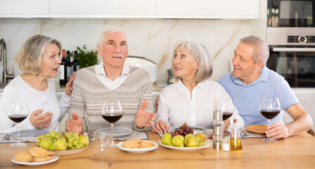 Group of happy elderly people drink red wine and chat at festive table