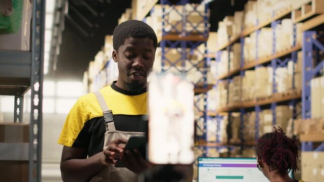 Black e-commerce worker filming a promotional video inside a fulfillment center, advertisement. Staff presenting products from warehouse racks, recording content for online shopping ads. Camera B.