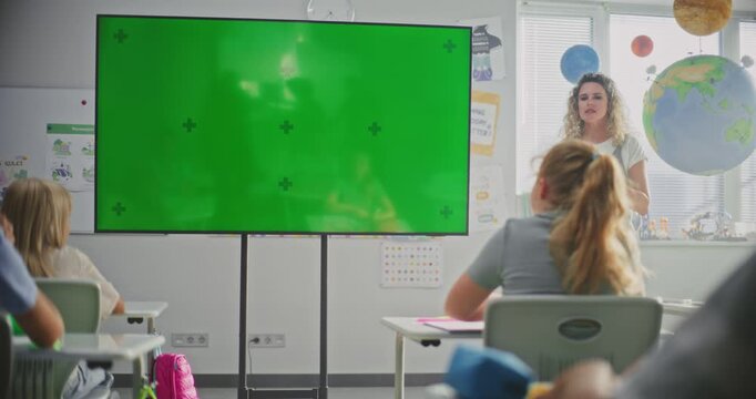 Female Teacher Educating Elementary School Students During Lesson in Modern Classroom. Large Digital Screen with Chroma Key. Green Screen Template for Educational Content or Interactive Visual Effects