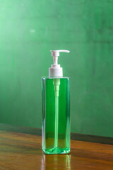 Green liquid soap dispenser bottle with pump on wooden table against green background, hygiene and cleanliness concept.