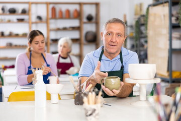 Satisfied mature man demonstrates pottery made by her own hands
