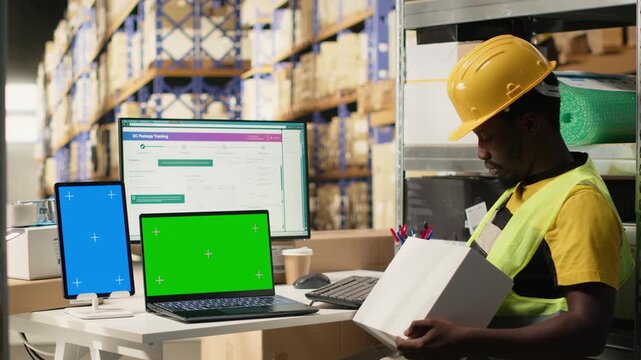 African american worker following shipments with tracking info next to copy space, warehouse operations with organized shelving and pallets. Accurate logistics and timely order dispatch. Camera B.