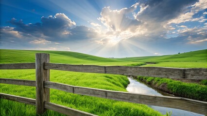 Fototapeta premium Weathered wooden fence stretching along lush green fields on rolling hill countryside farm, under cloudy blue sky with amazing sunlit rays effects