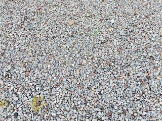 Gray gravel covers the ground, forming a seamless texture, usually used in construction or landscaping.  offers a uniform background. Between the pebbles, scattered small patches of green grass