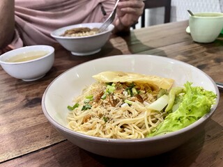 detail of a portion of chicken noodles with fried chips and lettuce isolated on white ceramic bowl on wooden table