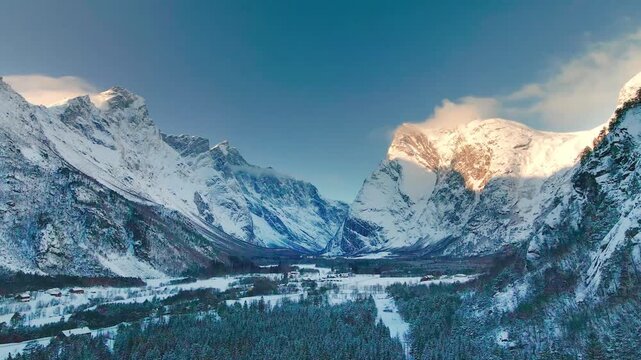 panoramic footage capturing the grandeur of Trollveggen, Norway, in winter. Featuring snow covered peaks, a serene valley, and a crisp blue sky, this footage evokes the raw beauty and scale of the Rom