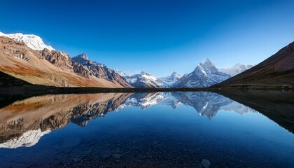 Fototapeta premium towering jagged mountains are mirrored in the calm clear water of a vast alpine lake beneath a bright blue sky