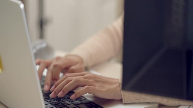 Macro shot of Asian woman typing on wireless keyboard, showing hand movement during office work or remote job task.