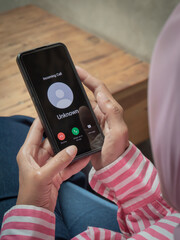 A woman holding a smartphone receiving an incoming call from an unknown number, showing the screen interface with decline and accept options