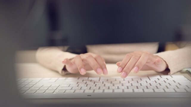Hands of Asian woman typing on a white wireless keyboard in soft lighting, representing digital workflow.