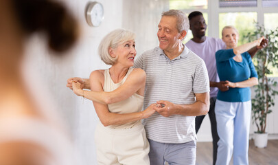 Obraz premium Mature male novice student of fitness studio practices paired Latin American rumba dance with elderly lady. Active hobby, movements to music, healthy lifestyle concept.