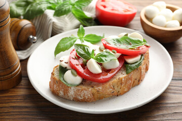 Delicious sandwich with mozzarella cheese, tomatoes and basil on wooden table, closeup