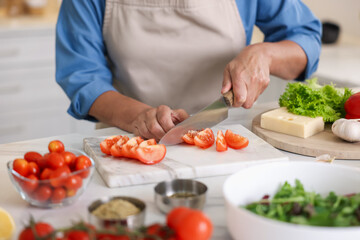 Senior woman cooking at white marble table in kitchen, closeup