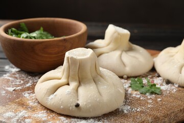 Uncooked khinkalis (dumplings), spices and parsley on wooden board, closeup