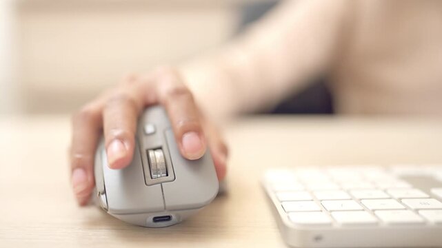 A close-up view of a hand clicking an ergonomic wireless mouse on a wooden work desk, symbolizing tech usage at the workplace.