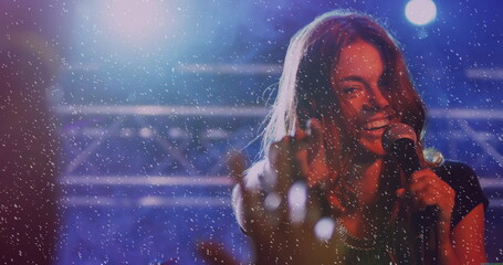 Reaching sleeveless singer singing into microphone on stage amid confetti under lights, copy space