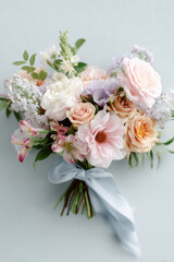 Elegant pastel bridal bouquet tied with a soft blue ribbon featuring blush and peach blooms