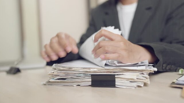 Close-up of hands flipping through a large stack of paperwork at a work desk. Represents busy office life, administration, and document management.