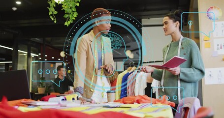 Designer leaning over examining colorful fabric swatch, partner arranging garments for fashion - Powered by Adobe