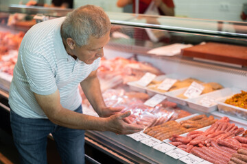 Adult man buyer in casual clothes chooses meat sausages in butcher shop..
