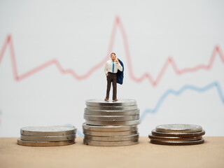 Mini toy of action figure at outdoor with blurred background. Miniature photography concept design. Minifigure of businessman character with market graph and money coin.