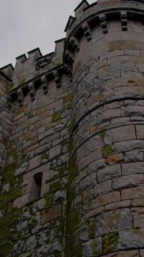 Stone walls and towers of an ancient castle rise against a cloudy sky, showcasing architectural details and the effects of time and weather