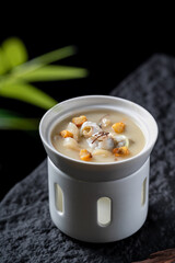 A cup of soup with various ingredients like nuts and slices, presented in a white container, looking appetizing and delicious.