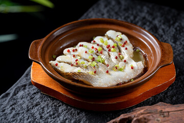 A plate of steamed fish fillet in a clay pot, garnished with colorful seasonings, presenting a delicious and appetizing appearance.