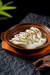 A plate of steamed fish fillet in a clay pot, garnished with colorful seasonings, presenting a delicious and appetizing look.
