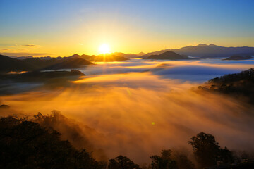 Obraz premium Golden light from the rising sun illuminates a stunning mountain landscape covered by a flowing sea of clouds.