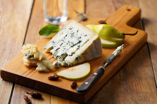 Delicious blue cheese and sweet green pear slices are arranged on a rustic wooden cutting board with a small knife.