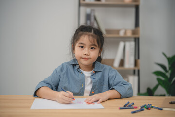 Naklejka premium Young girl engaged in creative drawing activity at home with colored crayons on a blank sheet of paper in a bright and minimalistic environment