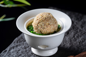 A delicious meatball is placed in a white bowl with green vegetables in soup, showcasing a appetizing and gourmet food presentation.