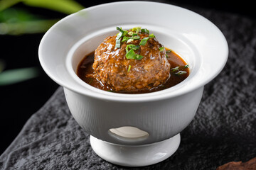 A delicious stewed meatball in a white bowl, covered with savory sauce and garnished with green herbs.