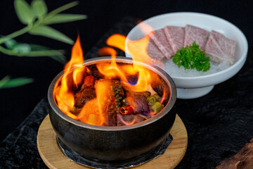 A bowl of food with flames and sliced meat beside it, showcasing a delicious and appetizing dish.