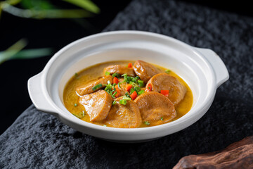 A bowl of braised taro root in aromatic soup, served in a white pot, showcasing tender taro and colorful seasonings.