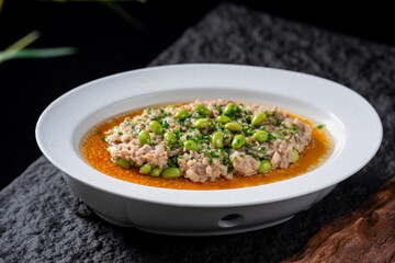 A plate of steamed minced pork topped with edamame, served in a white bowl with an orange broth.