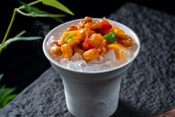 A cup contains a delicious cold dish with nuts and colorful vegetables, looking very appetizing and fresh.