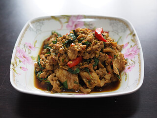 Thai stir-fried dish with minced meat, chili, and basil served on a floral porcelain plate, showcasing vibrant colors and rich texture.